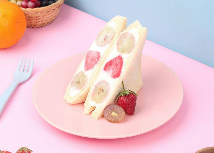 A fruit sandwich on a pink plate and table. The pinkness of its strawberry and grape filling is accentuated.